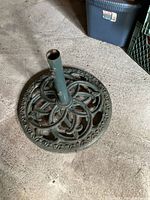 Top-down view of large cast iron umbrella stand showing ornate circular base and central metal tube with signs of wear.