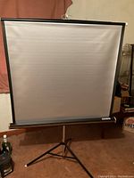 Front view showing the white projector screen mounted on a black tripod stand.