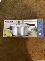 Photo of the Mirro pressure cooker box showing the product image, brand, and capacity information on a brown carpet background.