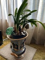 Large ornate porcelain planter with plant and decorative pine cones inside plastic insert