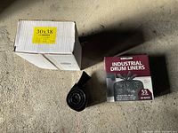 Photo of unopened Kirkland Industrial Drum Liners box (55 gallon, 60 bags), one rolled black bag and empty white box labeled 30x38