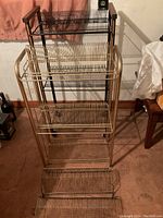Photo showing four metal record stands, one large freestanding rack with gold frame and three smaller standalone racks in black and gold finishes.