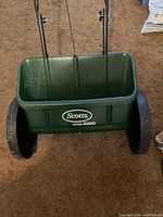 Front view of Scotts AccuGreen 1000 green plastic hopper seed spreader with large black wheels on each side.