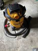 Yellow Shop-Vac wet/dry vacuum cleaner with attached hose and power cord, shown standing upright on a concrete floor.