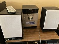 Full view of the audio system including the main CD/radio unit with two speakers and remote control on top of left speaker.