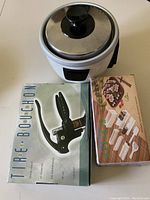 Top view of the rice cooker with sealed lid and the two boxed items: the sushi maker kit and the wine bottle corkscrew.
