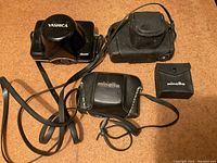 Top view of black camera cases and strap accessories including Yashica and Minolta branded cases