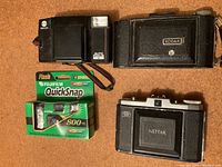 Four vintage cameras: Minolta Auto Focus V, Zeiss Ikon Nettar, Kodak folding camera, Fujifilm Quicksnap disposable camera in packaging