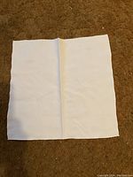 One white linen napkin laid flat on carpeted floor showing texture and fold crease.
