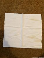 Single white linen napkin with green trim laid flat on carpeted surface.
