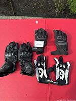 Three pairs of motorcycle gloves sized small in new condition, showing the top view of gloves laid out on red surface.