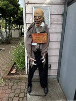 Full front view of the animatronic ghoul showing head, upper body, and hanging sign.