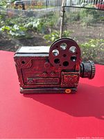 Front and side view of vintage cinema projector styled Halloween prop with red distressed paint and black lens