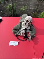 Front angled view of the crawling ghoul animatronic showing detailed skull, skeletal hands holding black chains, and worn dark green costume.