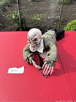 Full view of the crawling ghoul animatronic showing skull head, skeletal hands in chains, dressed in green and black tattered clothing with white collar.