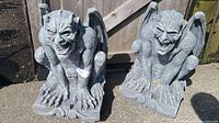 Front view of two gray gargoyle figures with detailed wings and claws, showing facial expressions and positioning.