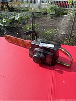 Photo of a Halloween chainsaw prop on a red table showing its orange blade and black and chrome handle.