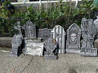 View of all Halloween graveyard decorations arranged together outdoors on pavement with garden background