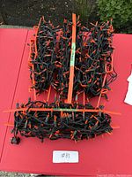 Two 25-foot double string Halloween lights with bright orange bulbs wound on orange plastic holders, shown laid out on a red surface with some greenery in the background.