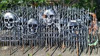Set of 9 black plastic Halloween lawn fence panels with silver skull designs, arranged outdoors on gravel ground.