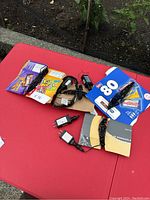 Lot of multiple Halloween string light sets arranged on red table, showing power adapters and packaging, with purple and orange bulbs visible
