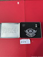 Top view of the open metal box showing the patch, pin, and miniature stein inside with foam insert.