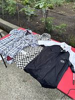 Photo of three men's short-sleeve shirts laid flat on red surface. Black Harley Davidson shirt, black and white Vans checkered shirt, blue and white Vans checkered shirt.