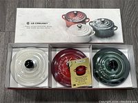 Box containing the three petite round casseroles in white, red and green with lids and tags.