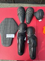 Photo showing assorted motorcycle gear pads including a large back protector, two knee pads, two elbow pads, and a smaller round pad.