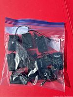 Eight black plastic animatronic remote controllers with wired connectors, showing Spirit Halloween branding on several units, stored inside a clear resealable plastic bag on a red background.