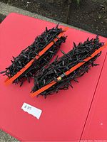 Four strands of purple Halloween lights wrapped on two orange plastic holders, shown on a red surface outdoors.