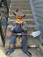 Full view of the animatronic scarecrow sitting on concrete stairs holding a shovel