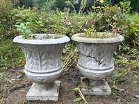 Front view of two cement planters side by side on the ground with surrounding vegetation