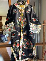Full view of the black kimono showing floral embroidery on front, sleeves and lower area with yellow piping and decorative closures.