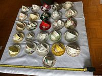 Overview of the entire collection of various vintage teacups and saucers laid out on a white cloth, showing multiple colors and patterns.