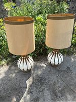 Full view of the two large Hollywood Regency style table lamps placed outdoors on pavement, showing their overall shape and lampshades.