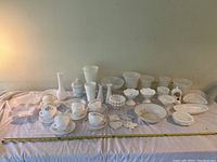 Wide shot of entire milk glass lot showing diverse pieces arranged on pink cloth with measuring tape for size reference.