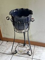Front angled view showing overall plant stand with blue ceramic pot, highlighting ruffled rim and metal legs.