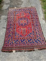 Full view of the old Persian rug laid on pavement showing overall condition and design.