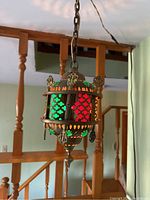 Front view of vintage swag lamp hanging from chain, showing colored green, red and orange glass panels within metal frame with decorative cutouts and hanging details.