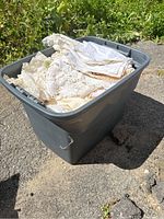 Large plastic storage tub filled with vintage lace and linen textiles, showing overall contents from an angle.