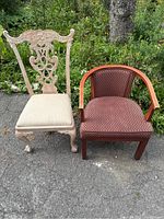 Two antique chairs side by side: one white carved chair with cushioned seat, one brown wooden armchair with patterned upholstery.