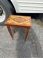 Full view of the wooden table with decorative top outside next to a tire.