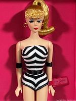 Close-up of Barbie doll's upper body showing detailed face, blonde ponytail, striped swimsuit, and Barbie by Mattel wrist tag