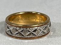 Front angled view of the ring showing textured silver with cross patterns and gold-lined edges.
