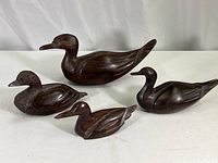 Four hand carved hardwood duck figurines of varying sizes laid out on white background.