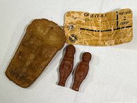 Full view of two red clay figurines with worn leather pouch and attached mailing tag