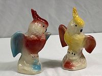 Two colorful mid-century ceramic parrot figurines photographed together on white background, showing full bodies and colors.