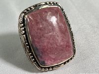 Front view of sterling silver ring with rectangular natural rhodonite cabochon stone in bezel setting with dotted silver border.
