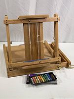 Wooden tabletop easel open, showing adjustable vertical supports and included pastels on front